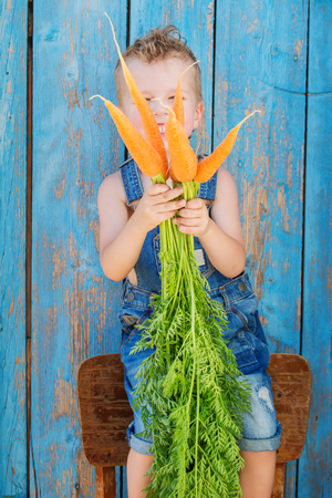 Funny little boy holding a bunch of carrots on a blue wooden backgroundの写真素材