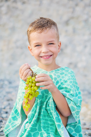 Happy child with grapes on vacation wrapped in a towel on the beachの写真素材