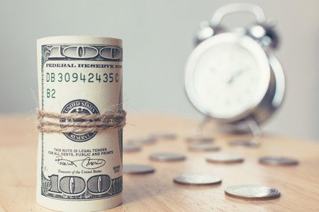 Roll money dollar banknote with coins and clock on table, American US currency billsの写真素材