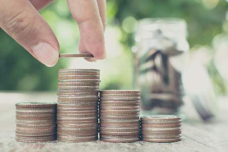 Hand putting coin stack with blurred background jar and green leaf, Save money and investment...