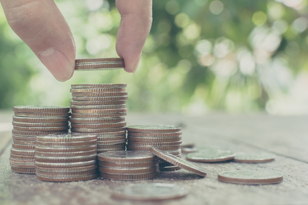Hand putting coin stack with blurred background and green leaf, Save money and investment conceptの写真素材