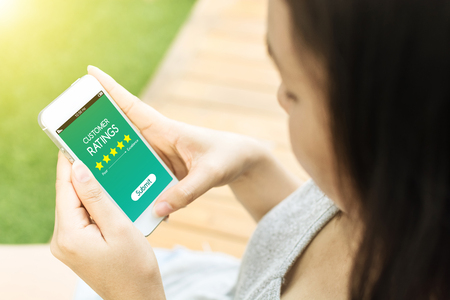 Asian woman hand holding mobile phone with customer ratingsの写真素材
