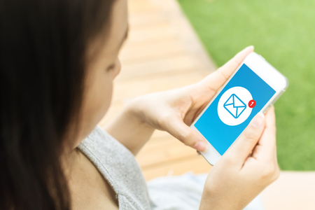 Asian young woman hand holding mobile phone with email message icon on screenの写真素材