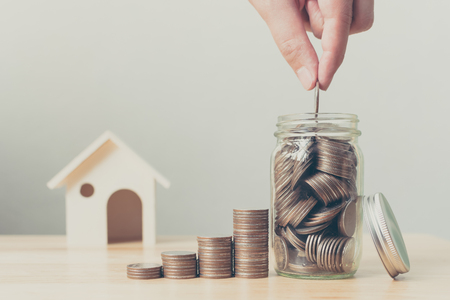 Property investment and house mortgage financial concept, Hand putting money coin stack with wooden houseの写真素材