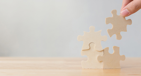 Hand of male or female putting jigsaw puzzle connecting on wooden desk and wall background, Strategic management and business solutions for successの写真素材