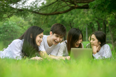 Asian group of friends talking and laughing with using laptop in green lawn in the parkの写真素材