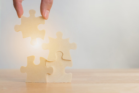 Hand of male or female putting jigsaw puzzle connecting on woodden desk, Strategic management and business solutions for successの写真素材
