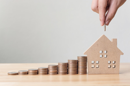 Property investment and house mortgage financial concept, Hand putting money coin stack with wooden houseの写真素材