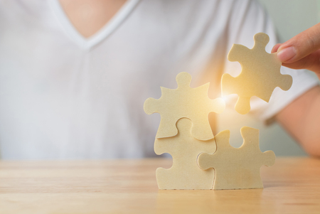 Strategic management and business solutions for success, Hand of male putting jigsaw puzzle connecting on woodden deskの写真素材