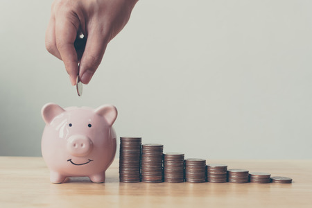 Hand of male or female putting coins in piggy bank with money stack step growing growth saving money. Concept finance business investmentの写真素材