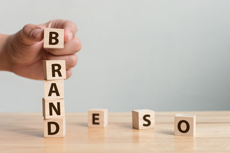 Hand of male putting wood cube block with word âBRANDâ on wooden table. Brand building for success conceptの写真素材