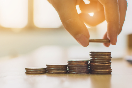 Hand putting coin stack step staircase on desk. Save money and investment conceptの写真素材