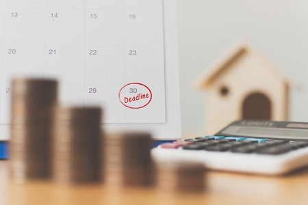 Tax payment season and finance debt collection deadline concept. Money coins stack, calendar, calculator and wooden houseの写真素材