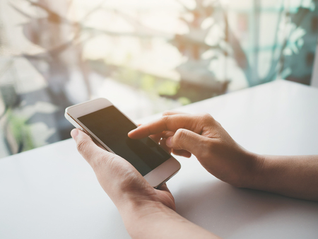 Mockup image of woman hand holding and touching white mobile phone with blank screen black colour smartphoneの写真素材