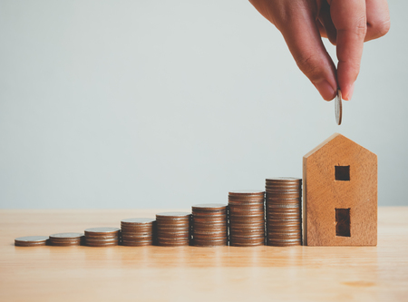 Property investment real estate and house mortgage financial concept, Hand putting money coin stack with wooden houseの写真素材