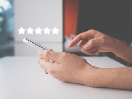Woman hand using smart phone with icon five star symbol to increase rating of company conceptの写真素材