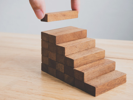 Hand arranging wood block stacking as step stair. Ladder career path concept for business growth...