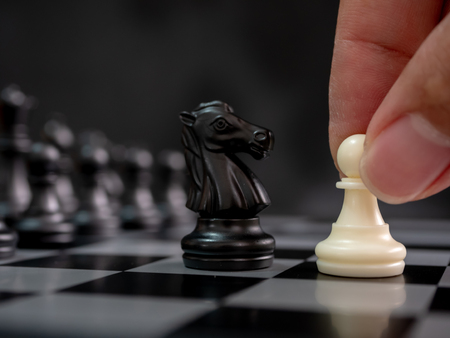 Strategic planning business competition concept. Hand holding white pawn moving playing chess board game. Leader and teamwork to successの写真素材