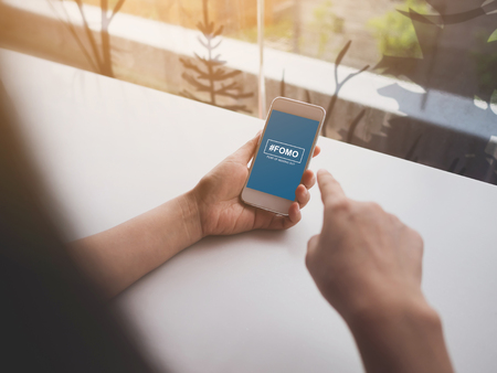 FOMO, fear of missing out concept. Female hand holding smartphoneの写真素材