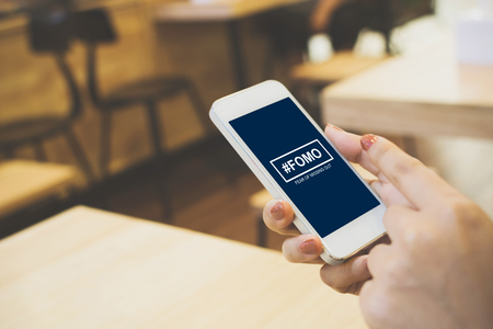 FOMO, fear of missing out concept. Female hand holding smartphoneの写真素材