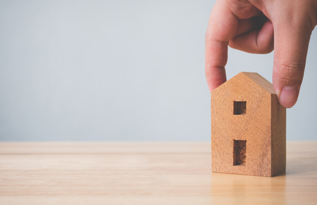 Property investment real estate and house mortgage financial concept. Hand holding wooden home on tableの写真素材