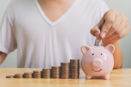 Hand of male putting coins in piggy bank with money stack step growing growth saving money. Concept finance business investmentの写真素材