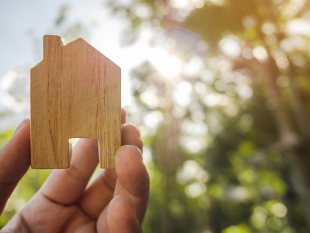Hand holding wooden house with green forest background blurred and sun lightingの写真素材