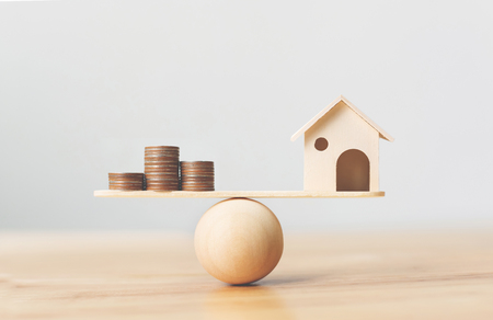 Wooden home and money coins stack on wood scale. Property investment and house mortgage financial real estate conceptの写真素材