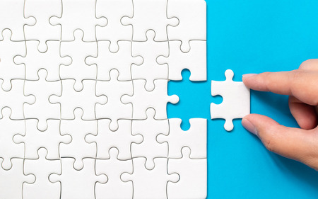 Hand putting piece of white jigsaw puzzle on blue background. Team business success partnership or teamwork.の写真素材