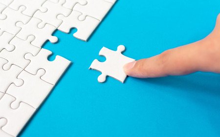 Hand putting piece of white jigsaw puzzle on blue background. Team business success partnership or...