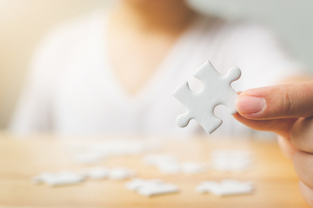 Hand of male trying to connect pieces of white jigsaw puzzle on wooden table. Healthcare for alzheimer disease, dementia, memory loss, autism awareness and mental health conceptの写真素材