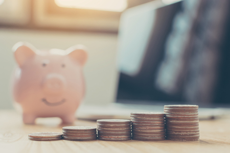 Saving money and investment concept. Money coin stack step staircase growing growth business with piggy bank, laptop on wood tableの写真素材