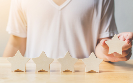 A man hand putting wooden five star shape on table. The best excellent business services rating customer experience conceptの写真素材