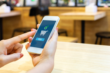 Concept online payment mobile technology. Hand of female using smartphone touching pay button mobile banking application in restaurantの写真素材