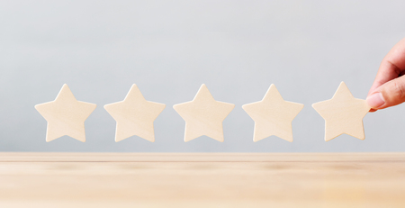 Hand holding wooden five star shape on table. The best excellent business services rating customer experience conceptの写真素材