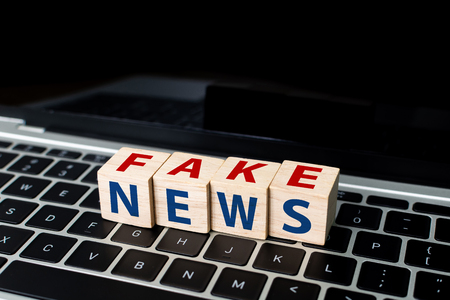 Wooden block cube shape with word FAKE NEWS on laptopの写真素材