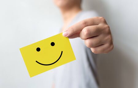Customer service experience and business satisfaction survey. Man holding yellow card with smiley faceの写真素材