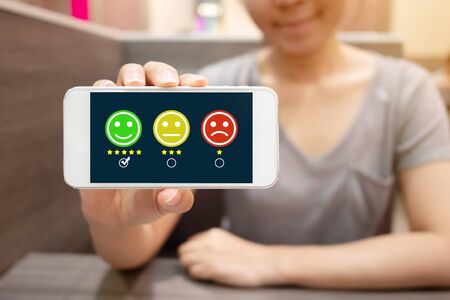 Customer Service Experience and Business Satisfaction Survey. Woman choose face smile on smart phoneの写真素材