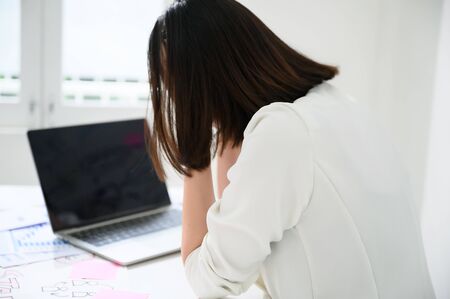 Young asian business woman upset or stressed feeling strain working on computer laptop in office room with paperwork document on deskの写真素材
