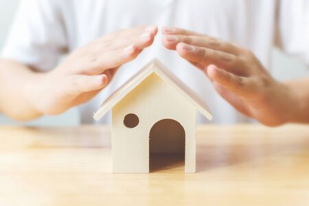 Insurance house and save money for property investment real estate concept. Man hand protect a big wooden home on tableの写真素材