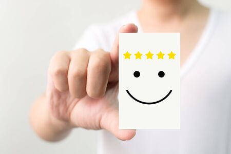 Customer service experience and business satisfaction survey. Man holding card with smiley face with five starの写真素材