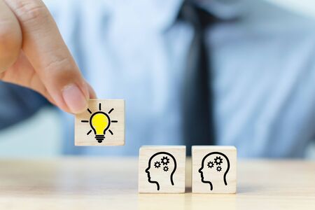 Concept creative idea and innovation. Hand picked wooden cube block with head human symbol and light bulb iconの写真素材