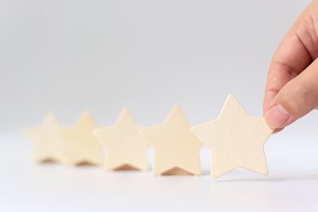 Hand putting wooden five star shape on white background. The best excellent business services rating customer experience conceptの写真素材