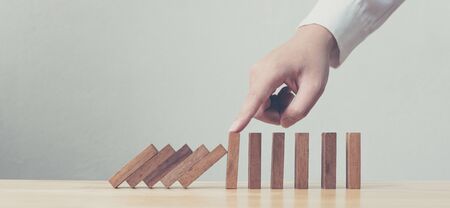 Hand stopping wooden domino business crisis effect or risk protection conceptの写真素材