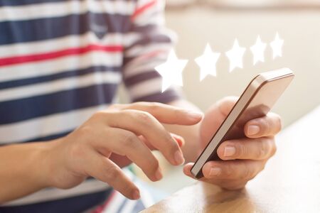Customer service experience and business satisfaction survey. Close-up image of male hands using mobile smart phone with icon five star symbol to increase rating of company conceptの写真素材