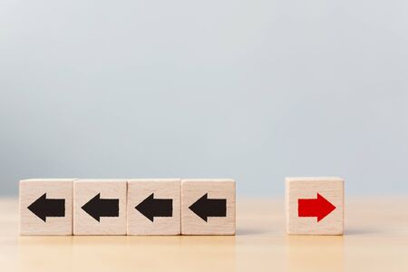Hand holding wooden block with red arrow facing the opposite direction black arrows, Unique, think...