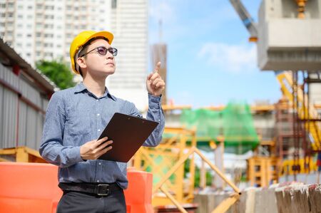 Young asian engineers are working on the construction site and surveying for making contour plans. Wear a yellow helmet safety. Hand holding paperwork documentの写真素材