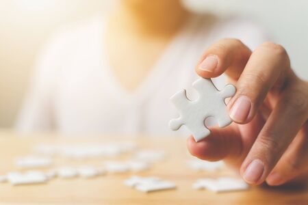 Hand of male trying to connect pieces of white jigsaw puzzle on wooden table. Healthcare for alzheimer disease, dementia, memory loss, autism awareness and mental health conceptの写真素材