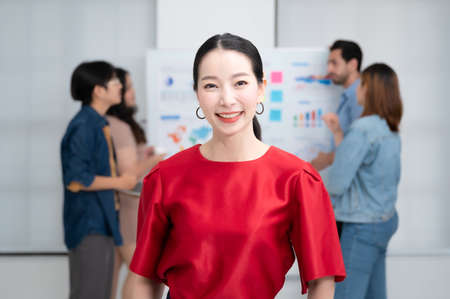 Confidence team leader. Young women asian owner startup business looking camera with smile while his colleagues working in the backgroundの写真素材