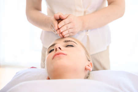 Beautiful woman receiving head and facial massage in spa salon. Concept of body health care and traditional thai massage relaxの写真素材